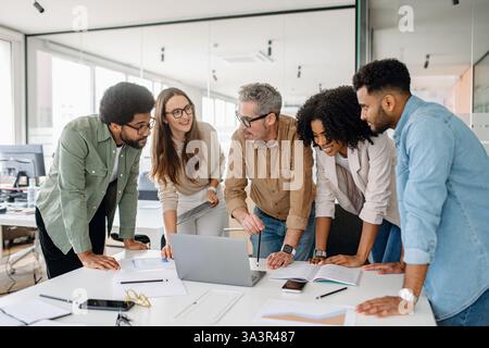 Multicultural business team discussing ideas in a modern office. A diverse group of professionals collaborating on a project, brainstorming strategies, and working together at a desk with documents Stock Photo