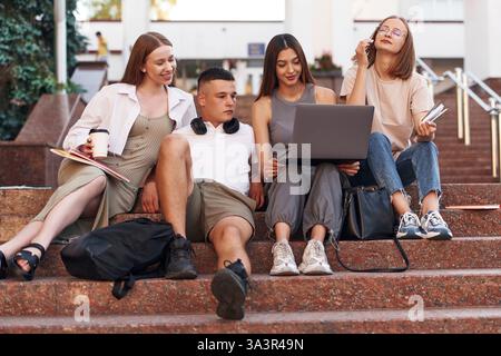 Learning, using laptop. Group of students are outside together. Stock Photo