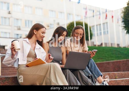 Learning, using laptop. Group of students are outside together. Stock Photo