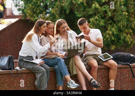 Learning, using laptop. Group of students are outside together. Stock Photo