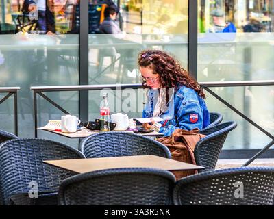 Young woman sitting at outdoor cafe table reading - Tours, Indre-et-Loire (37), France. Stock Photo