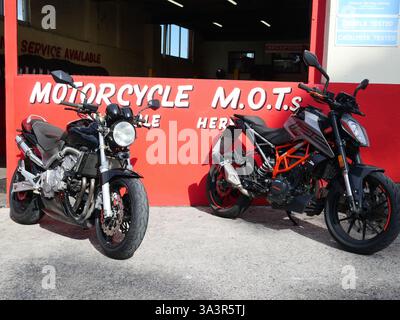 Two motorcycles parked outside a garage service centre for bike maintenance and motorcycle MOT Stock Photo