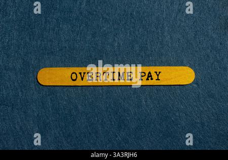 Overtime pay message written on yellow wooden stick on gray background. Conceptual overtime pay symbol. Copy space. Stock Photo