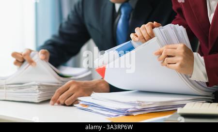 Two businesswomen are working together to search through important documents from a pile of documents on a table to verify the authenticity of the doc Stock Photo