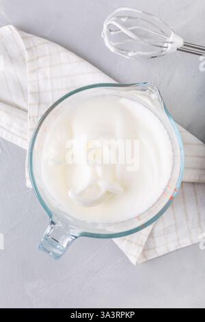 Close-up of a whisk and beaten egg whites to stiff peaks, a step in the