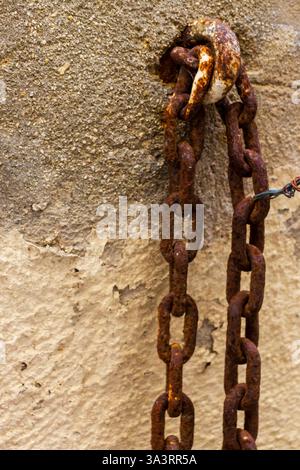 Old Rusty Chain Hanging on a Weathered Stone Wall Stock Photo