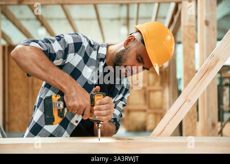 Drilling the hole in the wood. Industrial worker in warehouse, building the house. Stock Photo