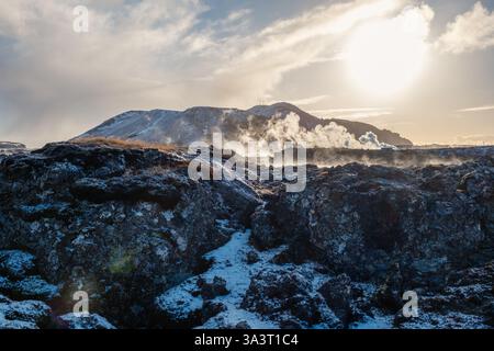 A landscape of the hardened lava field near the Blue lagoon area with the steam from the pools of the spa and the power plant rising into the low sun. Stock Photo