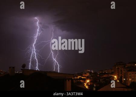 Dramatic lightning storm over a city skyline at night. Bright bolts illuminate the dark sky, creating a powerful and intense atmosphere Stock Photo