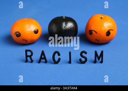 One black tangerine among orange ones and word Racism made with beads on blue background, closeup Stock Photo