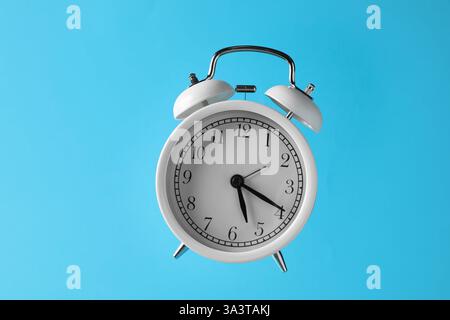 White alarm clock in air on light blue background Stock Photo