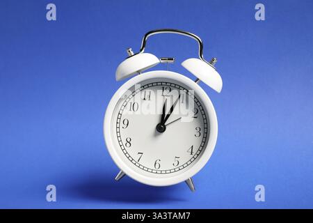 White alarm clock in air on blue background Stock Photo