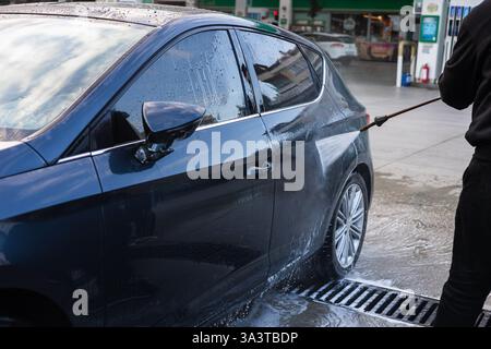 Person washes car with foam at an outdoor car wash facility on a sunny day Stock Photo