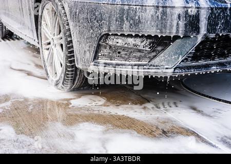 Person washes car with foam at an outdoor car wash facility on a sunny day Stock Photo