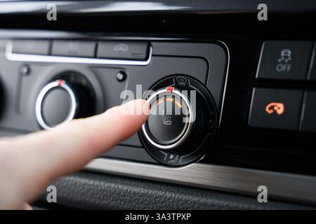 Finger about to press the heated seats button inside a car, the power is on full heat and the button is lit up Stock Photo