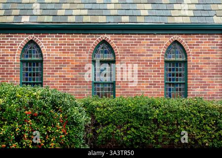 Small stained glass arched windows on side of red brick building Stock Photo