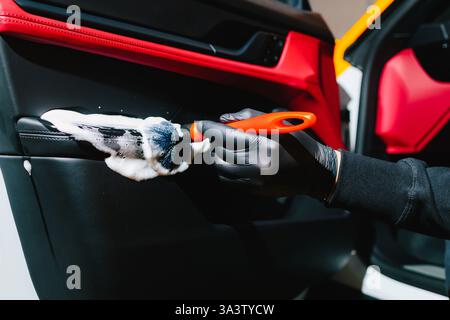 Car detailer cleans the auto door with foam brush and detergent. Process of removing dust and dirt from the car door panel at the carwash Stock Photo