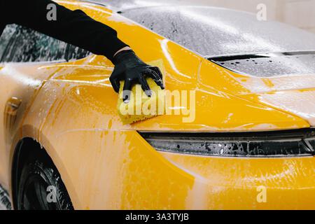 Man washes the sports car using a soapy solution and sponge before detailing procedure. Meticulous car detailing concept at the car service Stock Photo