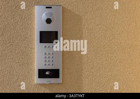 Modern intercom system with a built-in camera, keypad, and contactless access control panel mounted on a textured beige wall Stock Photo