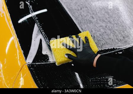 Man washes the sports car using a soapy solution and sponge before detailing procedure. Meticulous car detailing concept at the car service Stock Photo