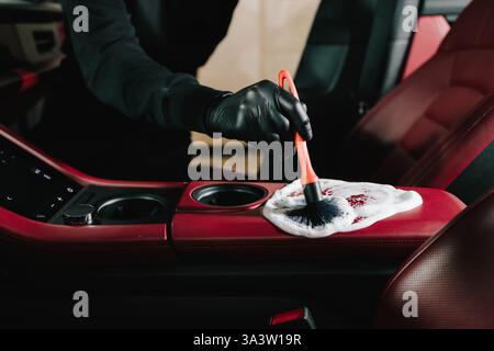 Car detailing process of cleaning leather auto interior with soap foam at the carwash. Man applies foam to the car's red leather for interior cleaning Stock Photo