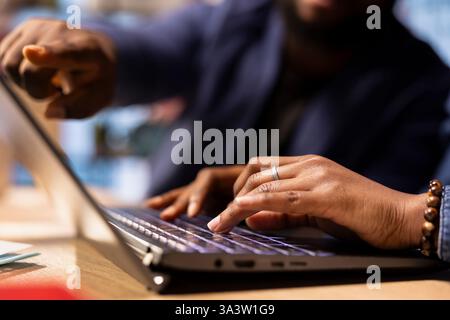 Black man and woman sits together in their cozy apartment space, discussing digital marketing strategy on a laptop. Supporting each other in their remote work and freelancing journey. Stock Photo