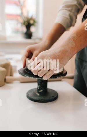 Artisan sculpts ceramic bowl using potter wheel. Hands shaping clay into dish in the craft studio Stock Photo