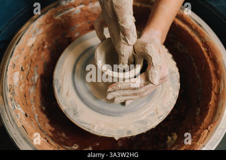 Female potter forms a clay product on a potter's wheel. Process of sculpting ceramic crockery in the manufacturing Stock Photo