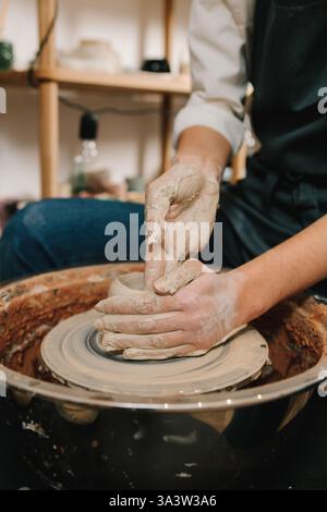 Female potter forms a clay product on a potter's wheel. Process of sculpting ceramic crockery in the manufacturing Stock Photo