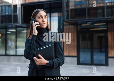 Confident female entrepreneur talking on mobile phone wearing stylish black formal clothes Confident female entrepreneur talking on mobile phone weari Stock Photo