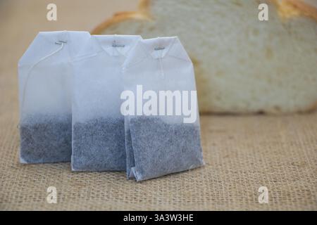 A close-up of three white tea bags with dark gray coloring inside, placed on top of burlap fabric. Stock Photo