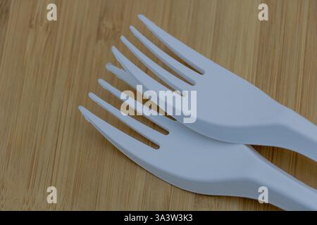Two white plastic fork pieces stacked on top of each other on a bamboo table, close-up. Stock Photo