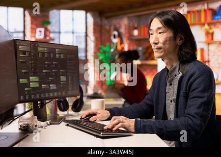 Senior technician coding advanced AI algorithm in startup office, refining machine learning models to enhance automation. Asian CTO manager using coding platform in Silicon Valley workplace Stock Photo