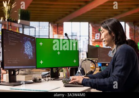 Software developer in pioneering technology startup using green screen computer to oversee artificial intelligence neural networks. Man in tech startup office using AI to build product on mockup PC Stock Photo