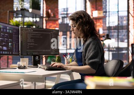 African american software engineer works on dual monitors and typing code for a development project. Technical developer multitasking, debugging and using advanced digital tools for coding. Stock Photo