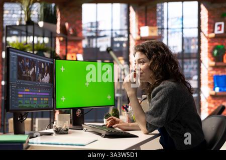 Woman video creator edits a multimedia project next to chroma key at agency office, using professional tech tools and editing software to manage timeline editing and video production. Stock Photo