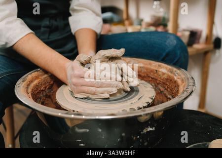 Female potter forms a clay product on a potter's wheel. Process of sculpting ceramic crockery in the manufacturing Stock Photo