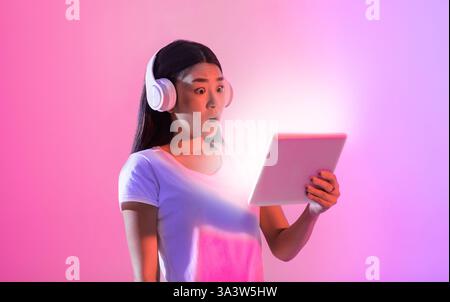 Young woman reacts with surprise while using a tablet in colorful lighting Stock Photo