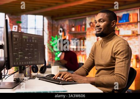 Happy man working in AI tech agency providing custom software development services. Cheerful african american IT expert using machine learning to streamline coding process in startup office Stock Photo