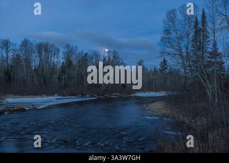 The full moon is setting over the West Fork of the Chippewa River on a March morning in northern Wisconsin. Stock Photo