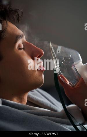 Man inhaling through oxygen mask for cough treatment. Using compressor nebulizer for disease treatment at home Stock Photo