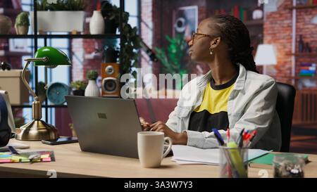 Fatigued woman daydreaming, gazing outside the window, feeling bored after working too much on job tasks. Contemplative person at home caught in thoughts, pondering, camera B Stock Photo