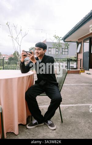 A young man enjoying mobile gaming in an outdoor setting. He's engrossed in the game on his smartphone, taking a break in a relaxed environment. The s Stock Photo