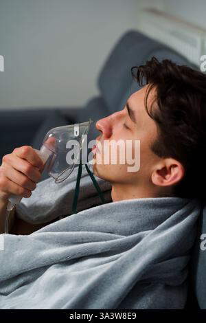 Man inhaling through oxygen mask for cough treatment. Using compressor nebulizer for disease treatment at home Stock Photo