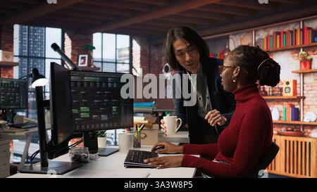 CTO supervisor in bringing coffee mug to tired worker debugging applications in artificial intelligence focused startup. Team leader helping overworked employee with caffeine beverage, camera A Stock Photo