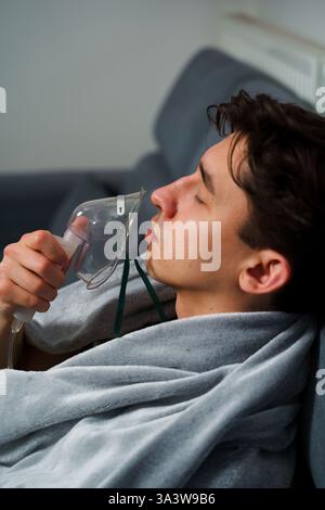 Man inhaling through oxygen mask for cough treatment. Using compressor nebulizer for disease treatment at home Stock Photo