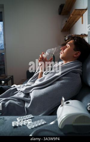 Man inhaling through oxygen mask for cough treatment. Using compressor nebulizer for disease treatment at home Stock Photo