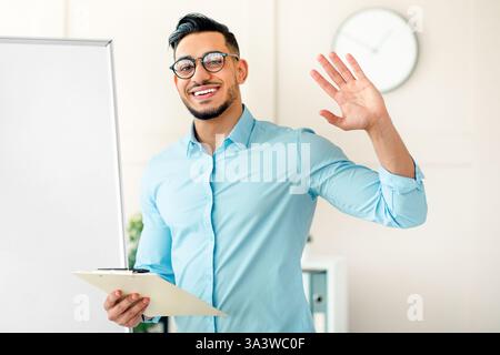 Young Arab businessman greeting while presenting in a corporate office setting Stock Photo