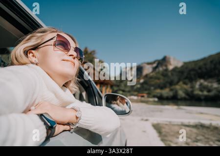 A smiling woman with sunglasses looks out of the window of a car, with ...