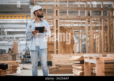 Unfinished project, holding digital tablet. Industrial worker in wooden warehouse. Stock Photo
